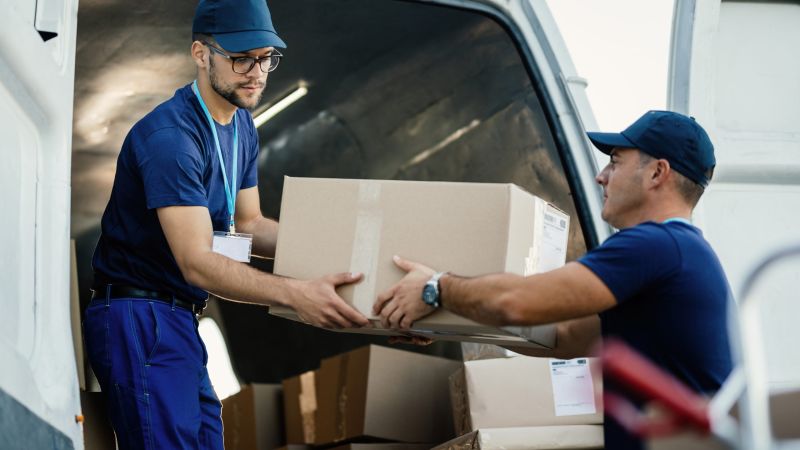 Young couriers cooperating while unloading packages from deliver